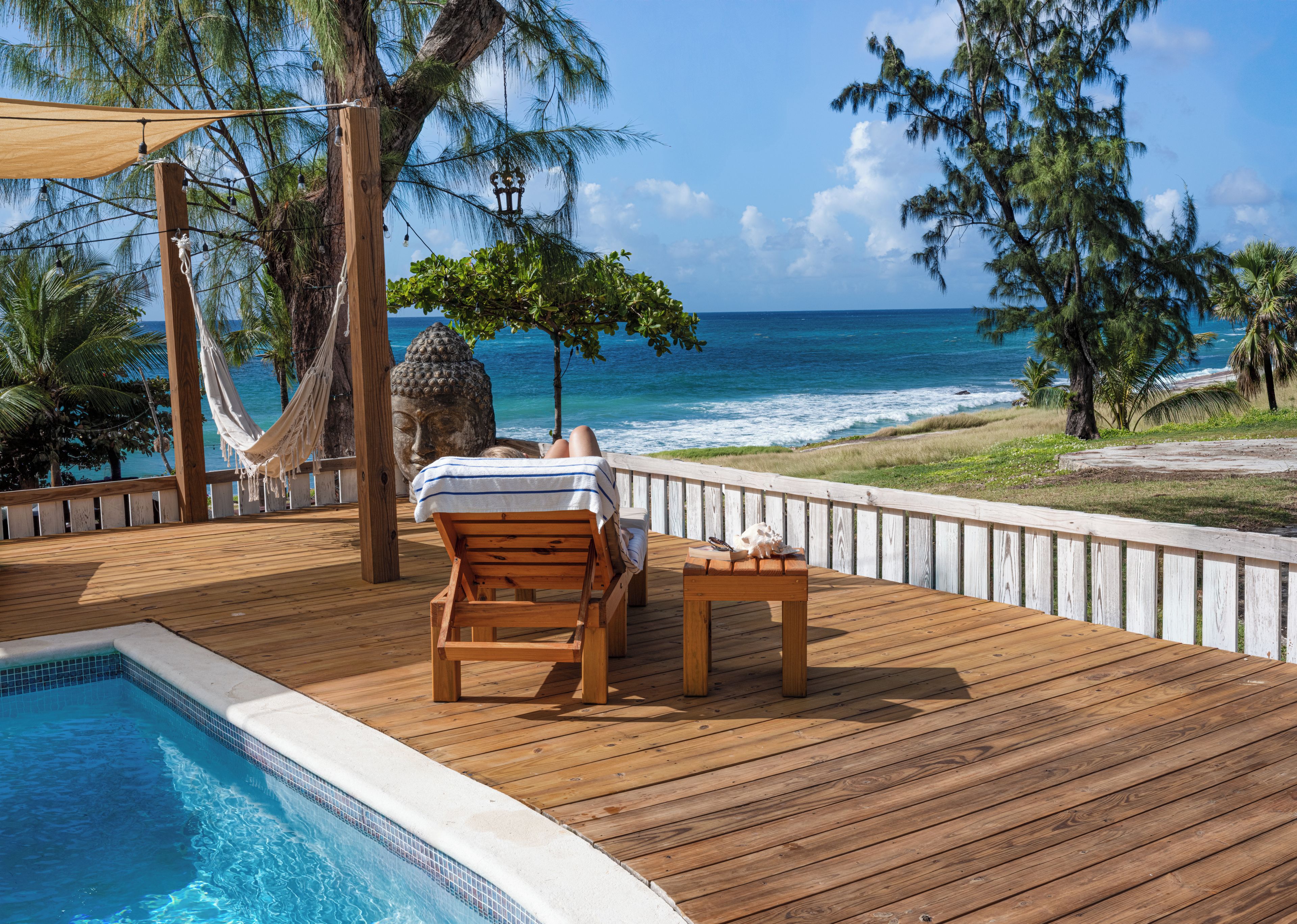 A wooden deck with a pool, a hammock, and a view of the ocean.