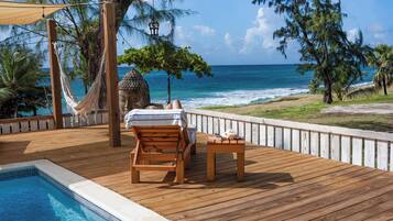 A wooden deck with a pool, a hammock, and a view of the ocean.