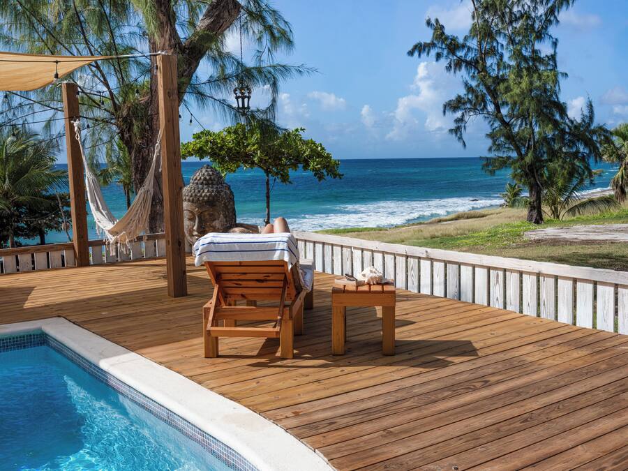 Une terrasse en bois avec une piscine, un hamac et une vue sur l’océan.