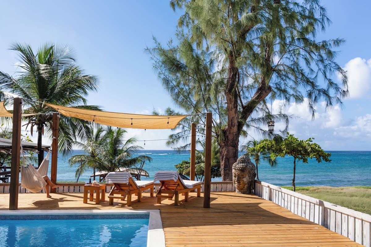 A wooden deck with lounge chairs and a pool, overlooking the ocean.