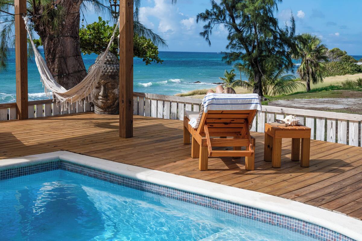 A wooden deck with a pool, a hammock, and a chair with a towel.