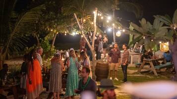 An outdoor gathering with people standing and conversing, surrounded by palm trees and string lights.