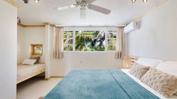 Un dormitorio con cama, ventana con cortinas, ventilador de techo y vistas a palmeras.