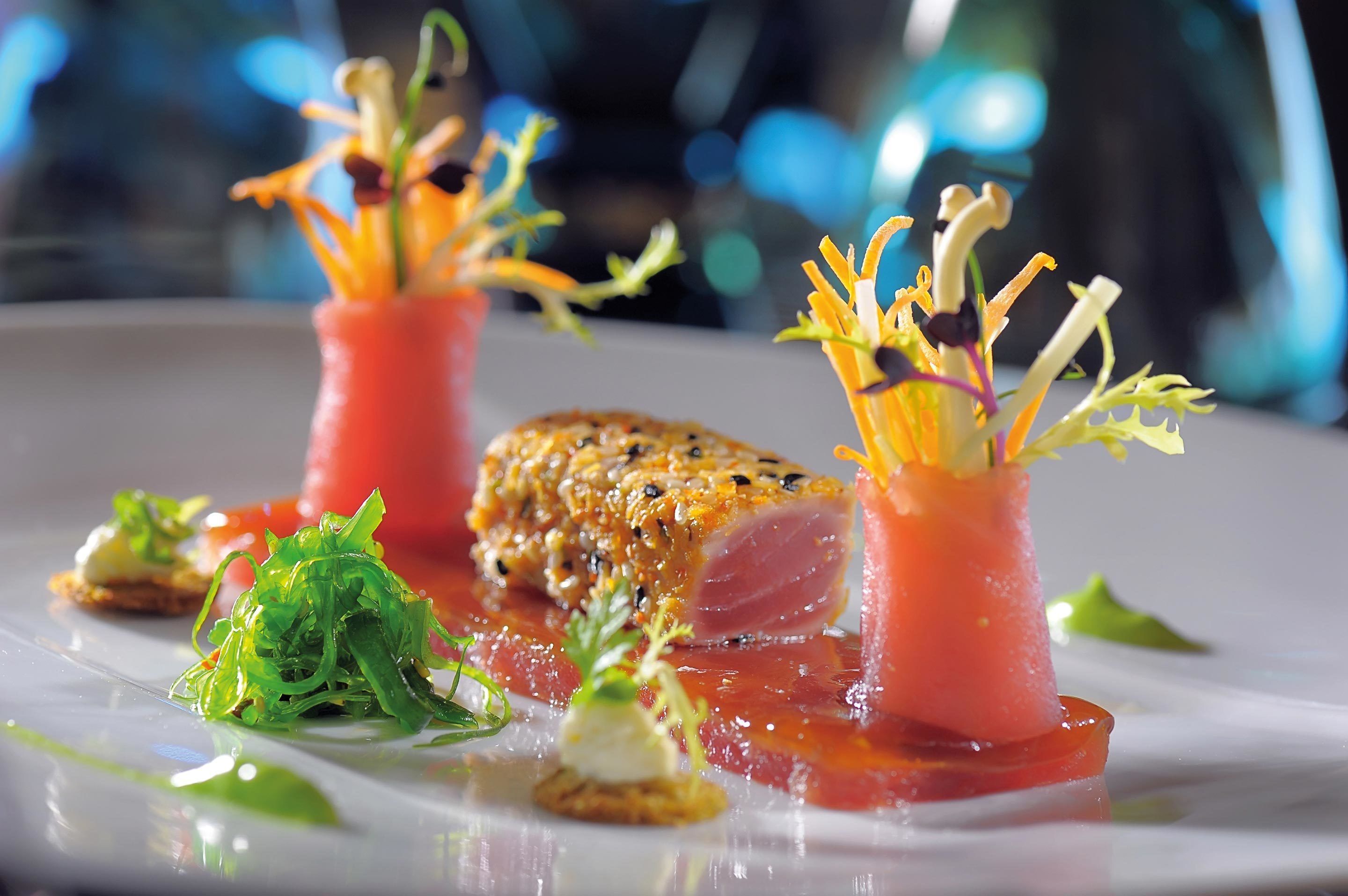 A dish with seared fish, garnished with microgreens and a pink sauce, on a white plate.