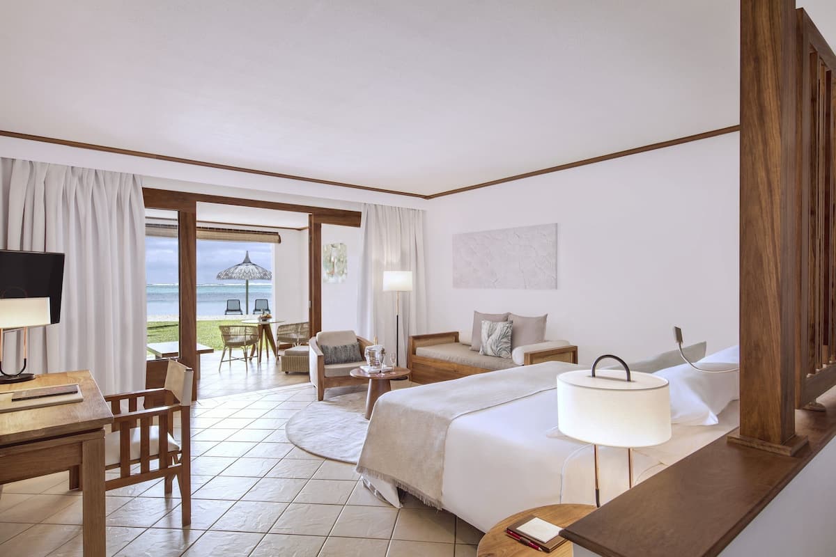 A hotel room with a bed, a desk, a chair, a lamp, and a view of the sea.