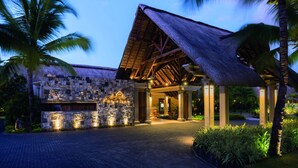 A resort entrance with a stone facade, a thatched roof pavilion, and a paved driveway. - Paradis Beachcomber Golf Resort & Spa (Le Morne)