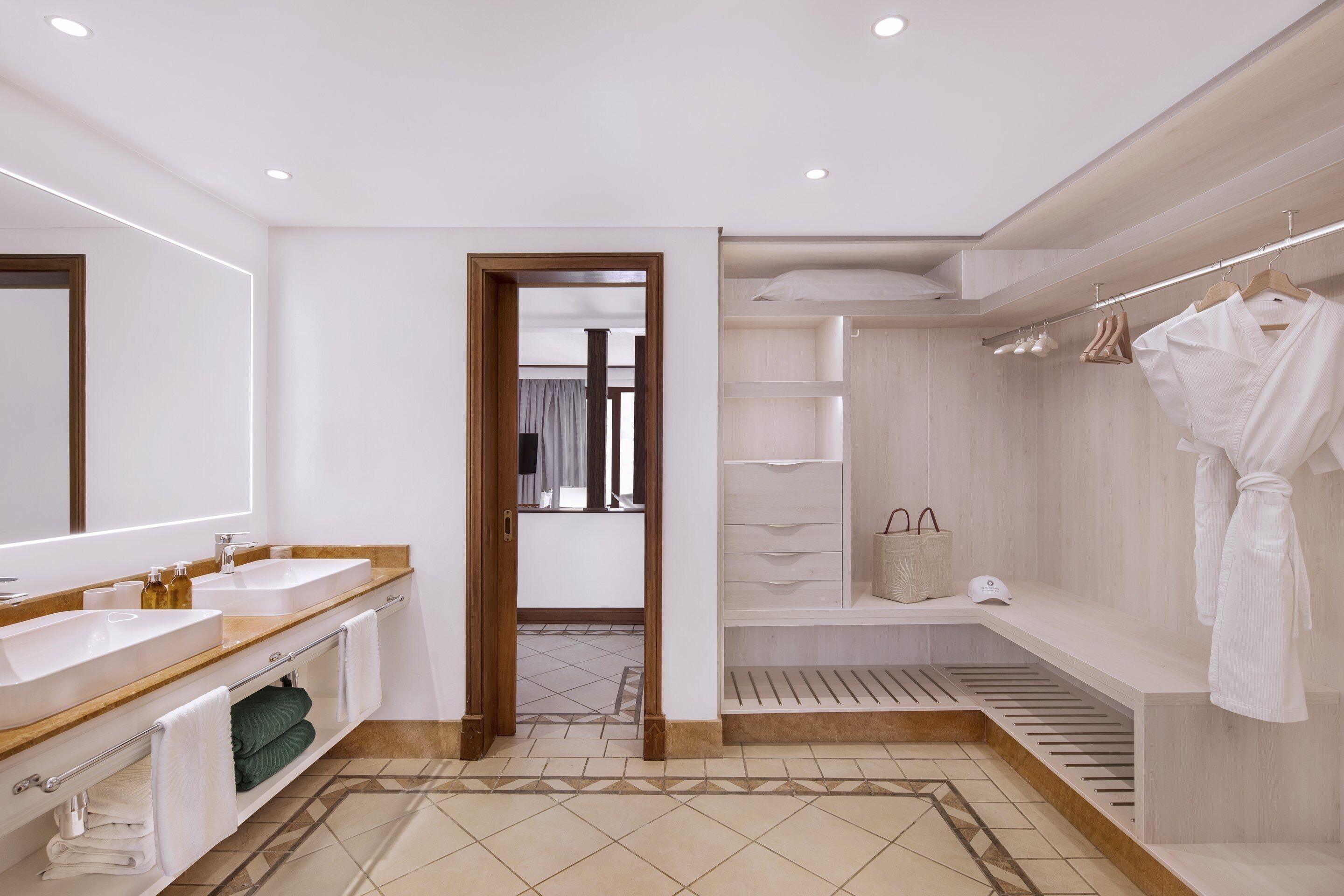 A modern bathroom with a large mirror, two sinks, a vanity, and a walk-in shower with a robe hanging.