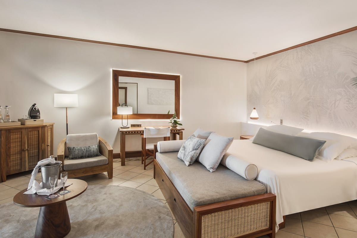 A modern hotel room with a large bed, a sofa, a desk, and a dining area.