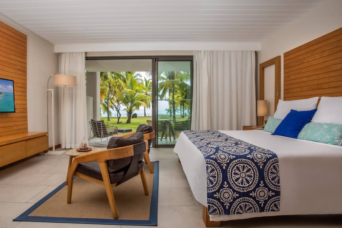 A hotel room with a bed, a desk, a chair, a TV, and a view of the beach.