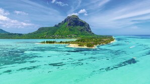 A tropical island with a prominent mountain, clear turquoise waters, and a small settlement. - Paradis Beachcomber Golf Resort & Spa (Le Morne)