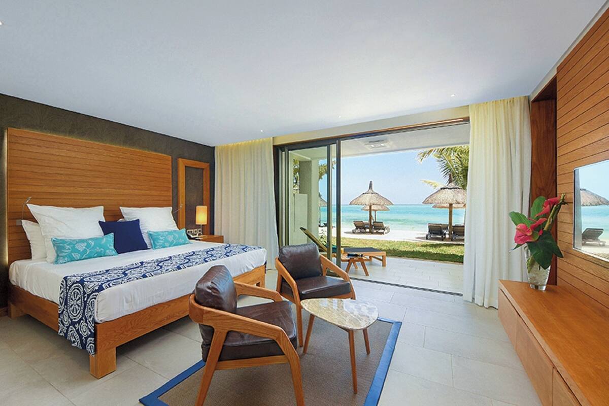 A hotel room with a bed, a desk, a chair, a small table, and a view of the beach.
