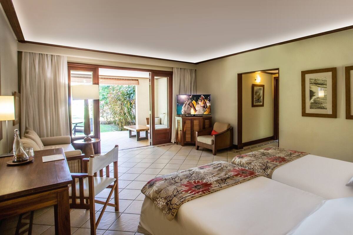 A hotel room with a bed, a desk with a lamp, a chair, a television, and a view of the outdoors.