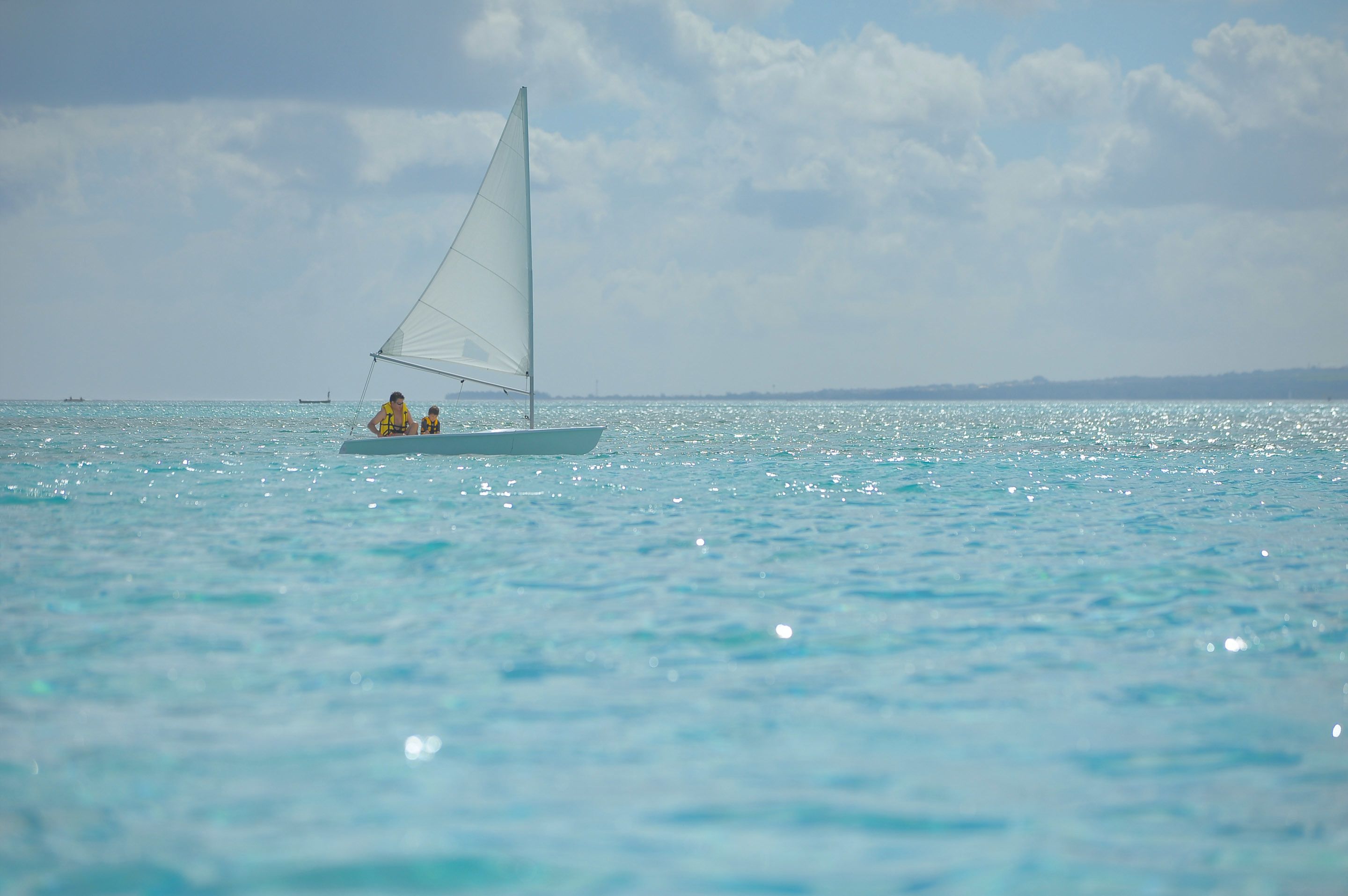 Un voilier sur des eaux turquoise et calmes, sous un ciel dégagé.