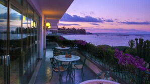 Ein Balkon mit Sitzgelegenheit im Freien, mit Blick auf ein Gewässer und einen Sonnenuntergangshimmel.