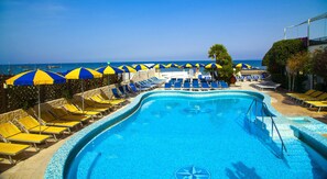 A pool area with blue and yellow sun umbrellas, lounge chairs, and a view of the sea. - Hotel Ambasciatori (Ischia)