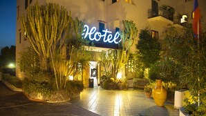 Ein Hotel Eingang mit einer Neonreklame, Kakteen und Topfpflanzen.