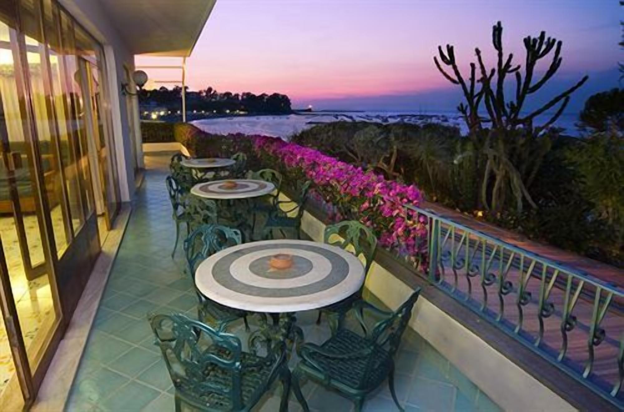 A terrace with outdoor seating and a view of the sea at dusk.