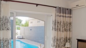 A hotel room with a bed, a small table, a chair, a ceiling fan, and a view of a swimming pool. - Mo Residence (Grand-Baie)