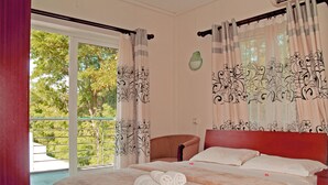 A bedroom with a large bed, a chair, and a view of greenery outside. - Mo Residence (Grand-Baie)
