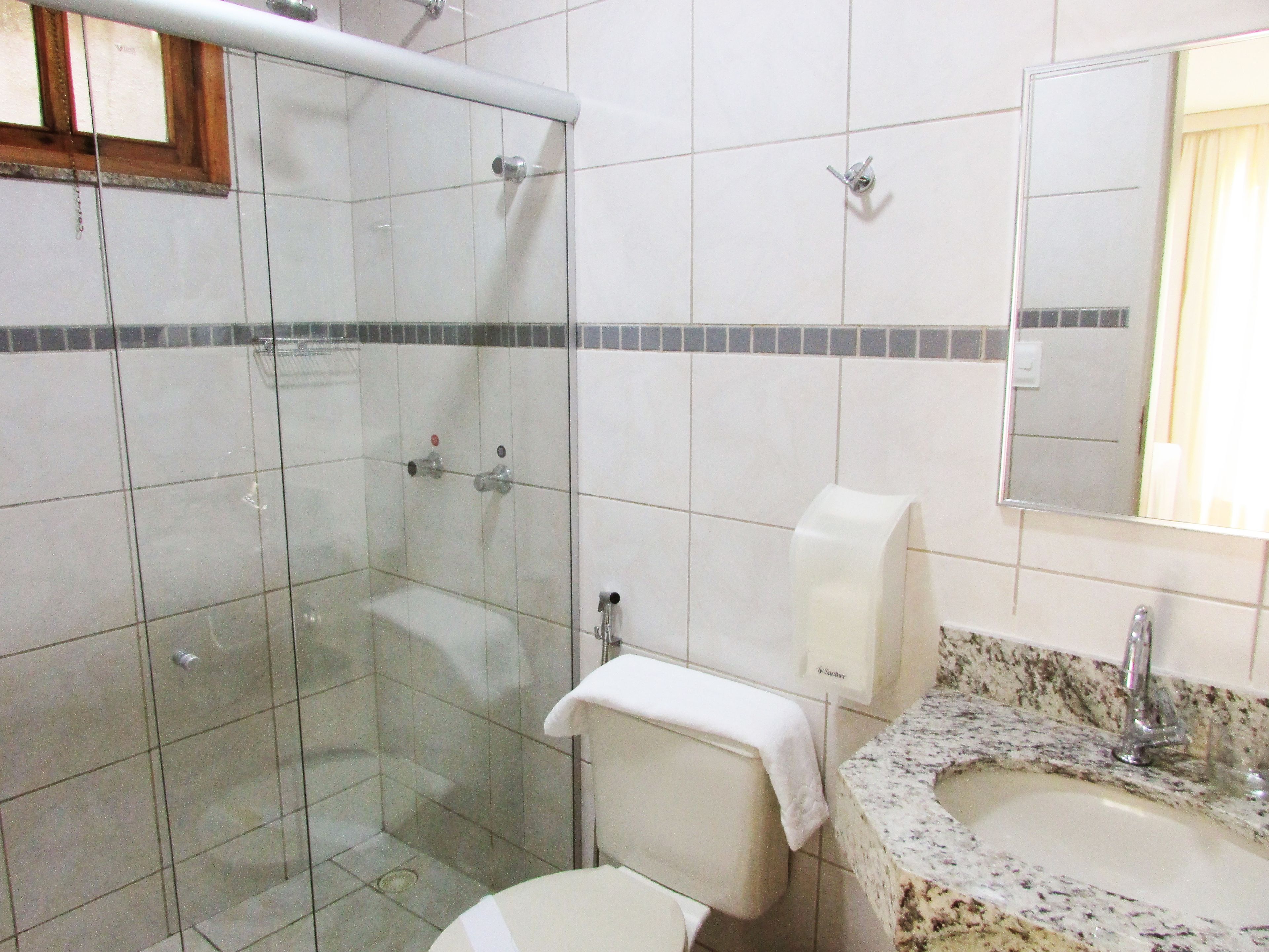 Un baño con cabina de ducha de vidrio, un inodoro, un lavabo con encimera de mármol y un espejo.