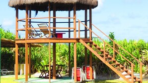 A wooden structure with a thatched roof, a staircase, and a seating area with chairs and a table. - Ilhéus North Hotel (Uruçuca)