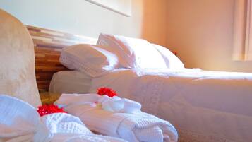 Quarto de hotel com duas camas, roupa de cama branca e cabeceira de madeira.