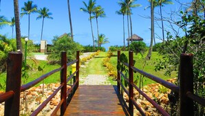 A wooden pathway leading through a tropical garden with palm trees and a clear blue sky. - Ilhéus North Hotel (Uruçuca)