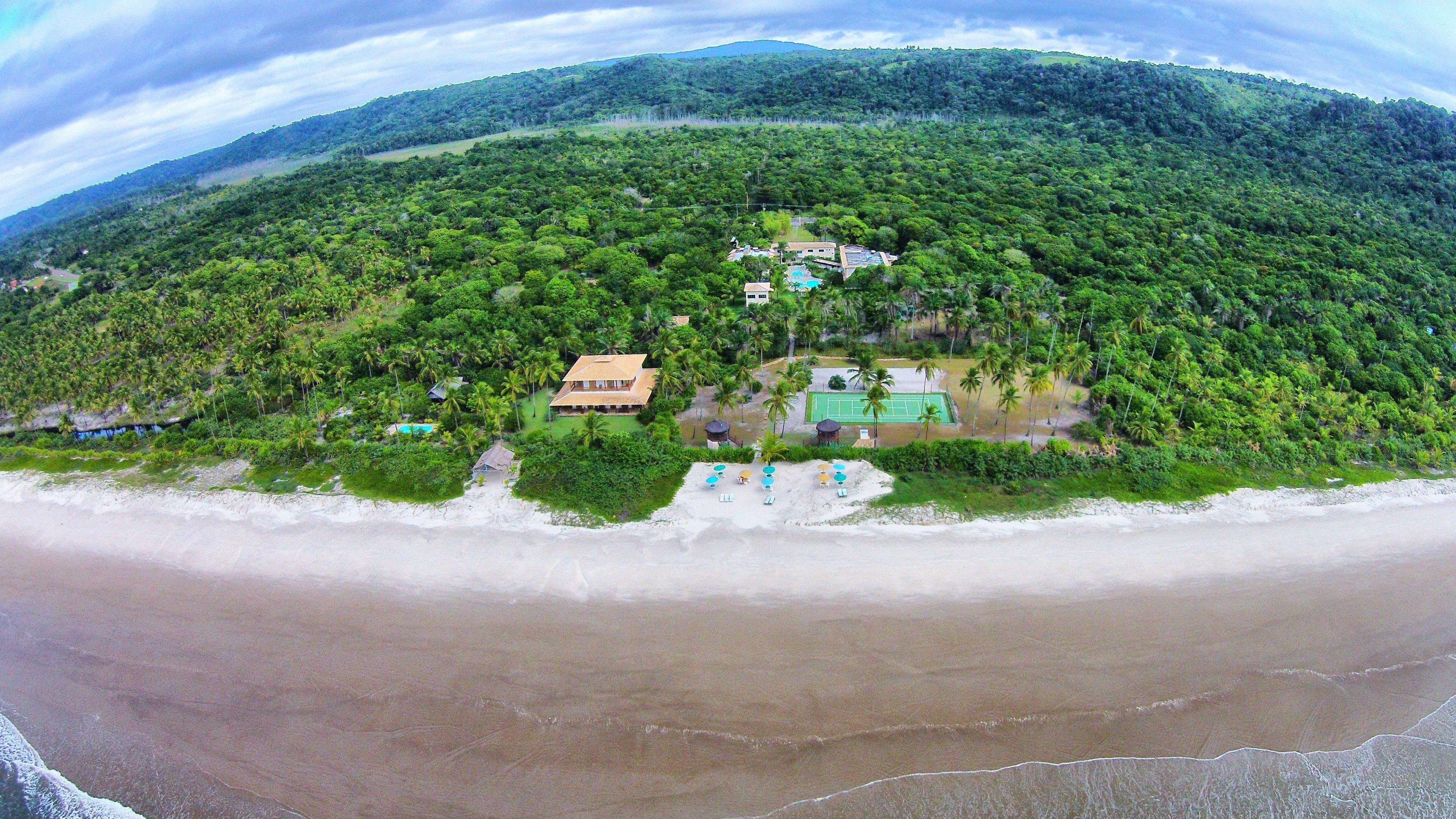 A tropical resort with a beach, palm trees, and a tennis court.