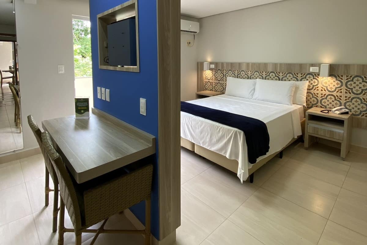 A modern hotel room with a bed, bedside table, and a desk with a chair.