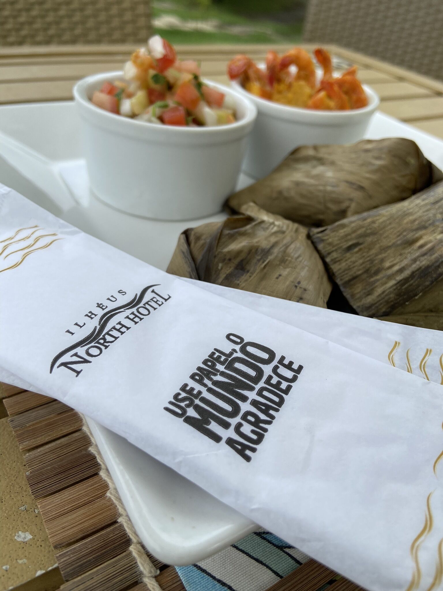 Uma bandeja com tamales e duas tigelas de molho de tomate, e um guardanapo com o texto "Use Papel, Mundo Gradee".
