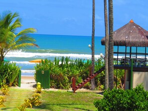 A beachside view with a thatched-roof structure, palm trees, and a clear view of the ocean. - Ilhéus North Hotel (Uruçuca)