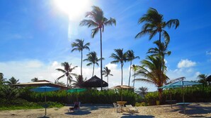 A beach with palm trees, a thatched-roof hut, and beach chairs under umbrellas. - Ilhéus North Hotel (Uruçuca)