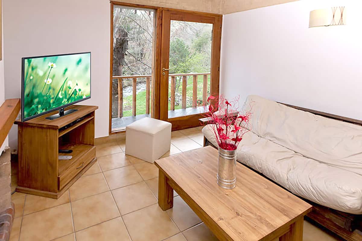 A living room with a TV, a white sofa, a wooden coffee table, and a glass vase with flowers.
