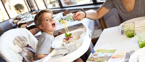 Un comedor con una trona, una mesa para dos personas y un ventanal con vistas al exterior.