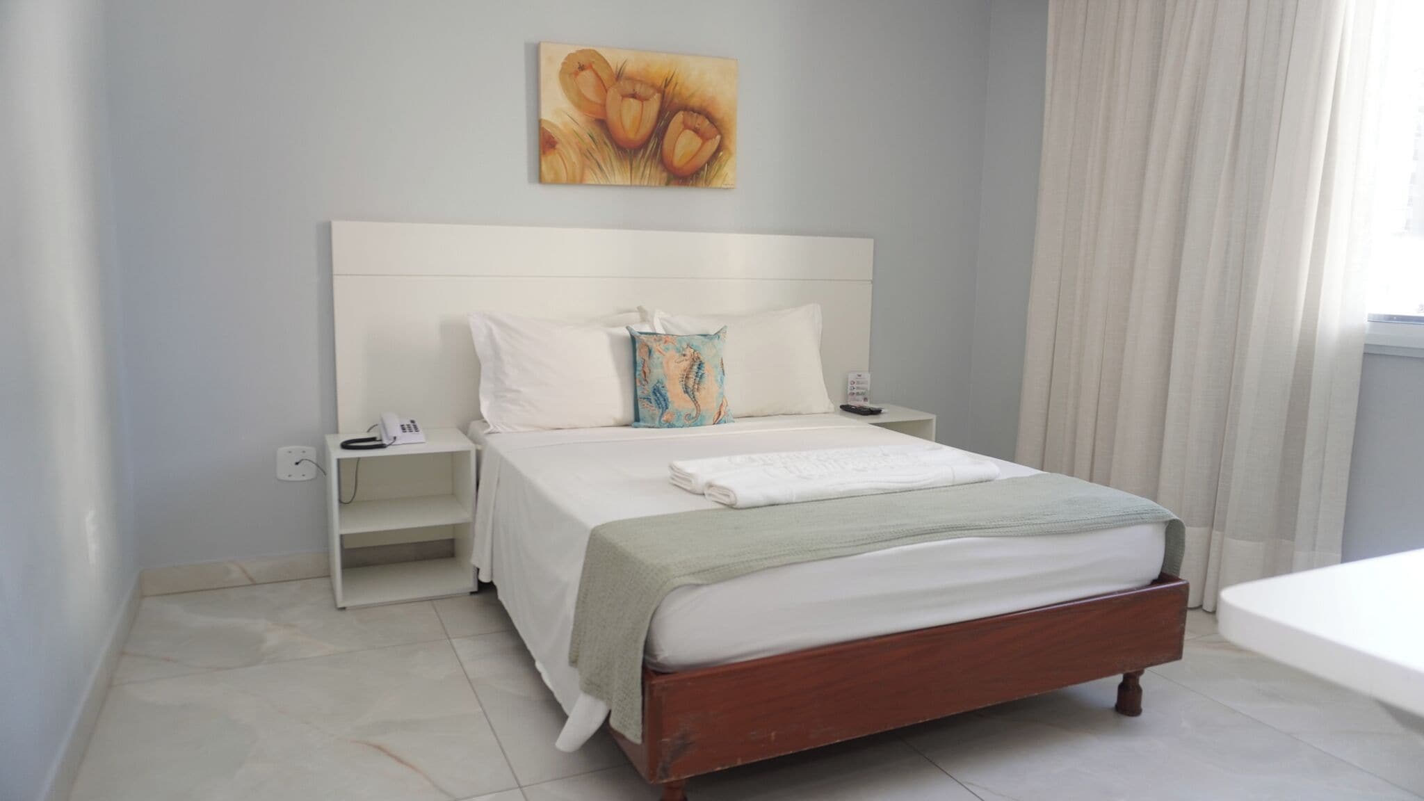 A hotel room with a wooden bed, white bedding, a bedside table with a phone, and a painting on the wall.