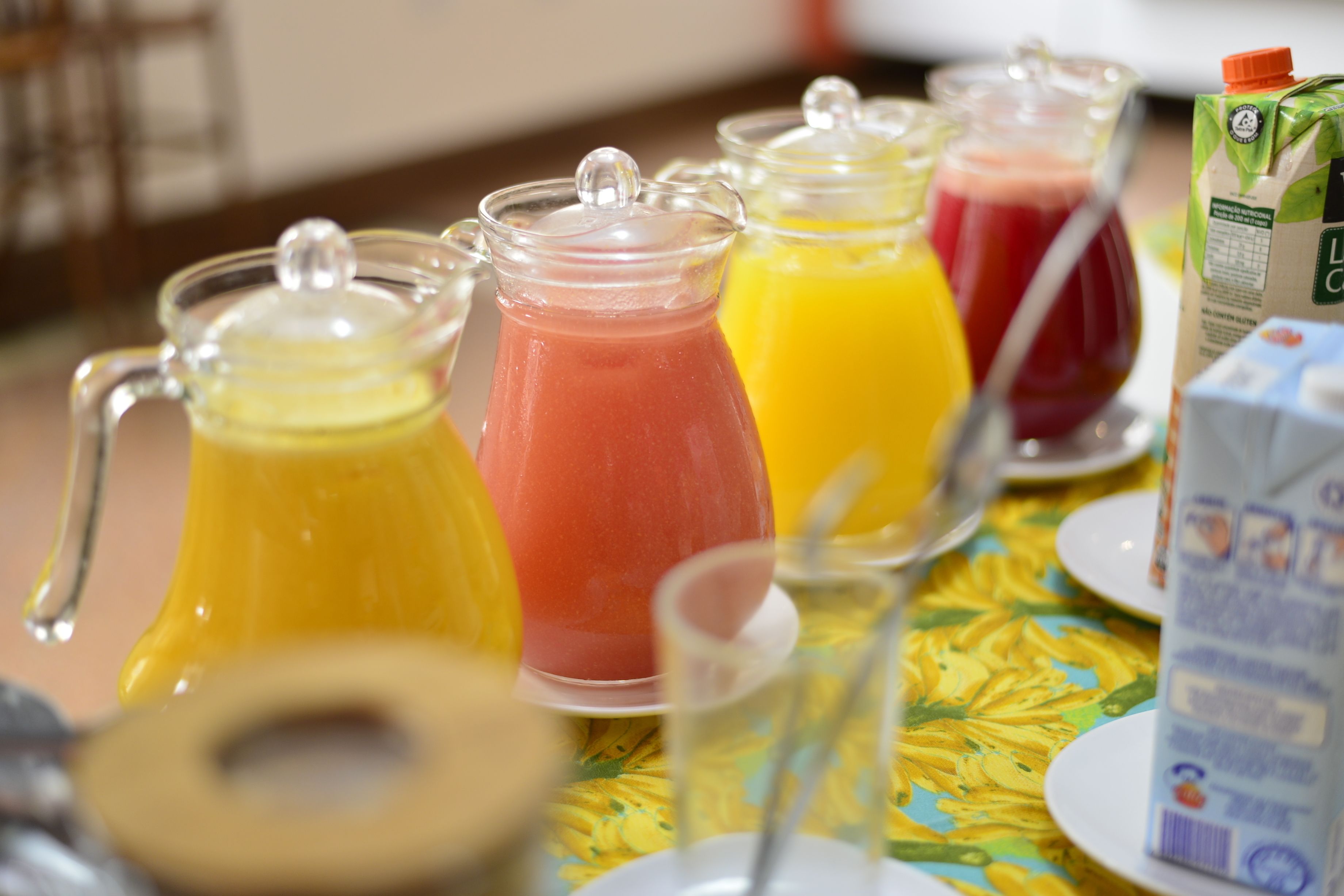 A breakfast table with various fruit juices in glass containers and a carton of milk.