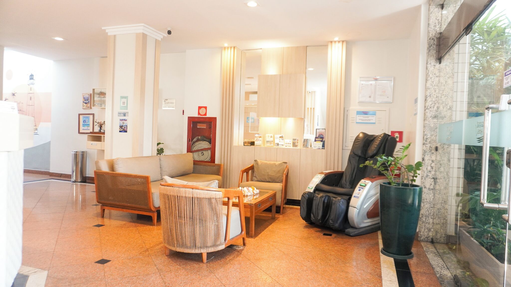 Eine Hotteillobby mit einer Rezeption, einer Sitzecke, einem Massagesessel und Blick ins Freie.