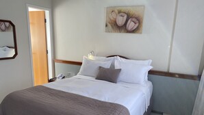 Una cama bien hecha con ropa de cama blanca y marrón, un teléfono en la mesita de noche y un cuadro con flores en la pared.
