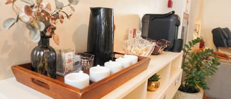 A reception area with a wooden tray holding various items, a vase with dried flowers, a black pitcher, and a coffee machine.