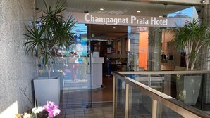 La entrada del Hotel Champagnat Praia, con baranda de cristal y orquídeas en macetas.