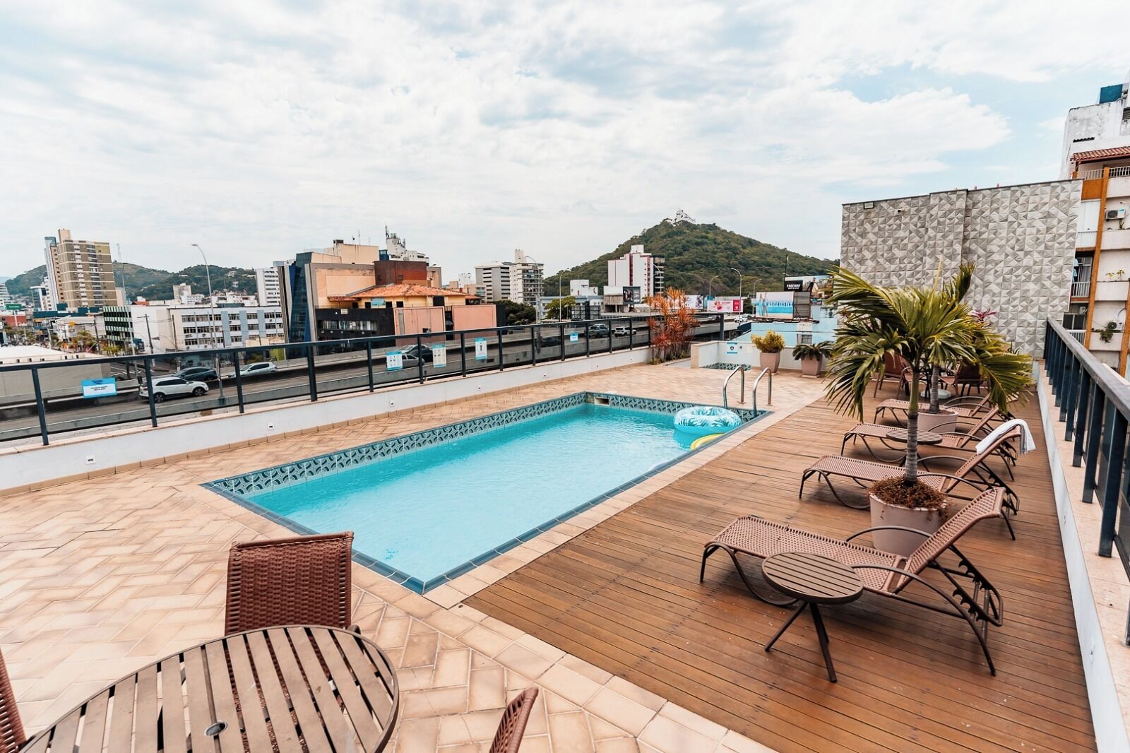 Zona de piscina en la azotea con vistas a la ciudad y una colina al fondo.