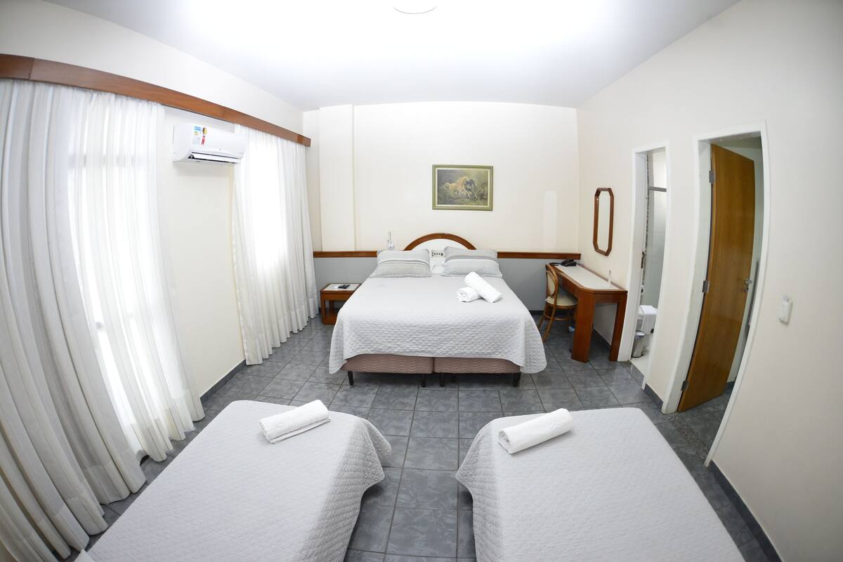 A hotel room with two beds, a desk, a chair, a mirror, and an air conditioning unit.