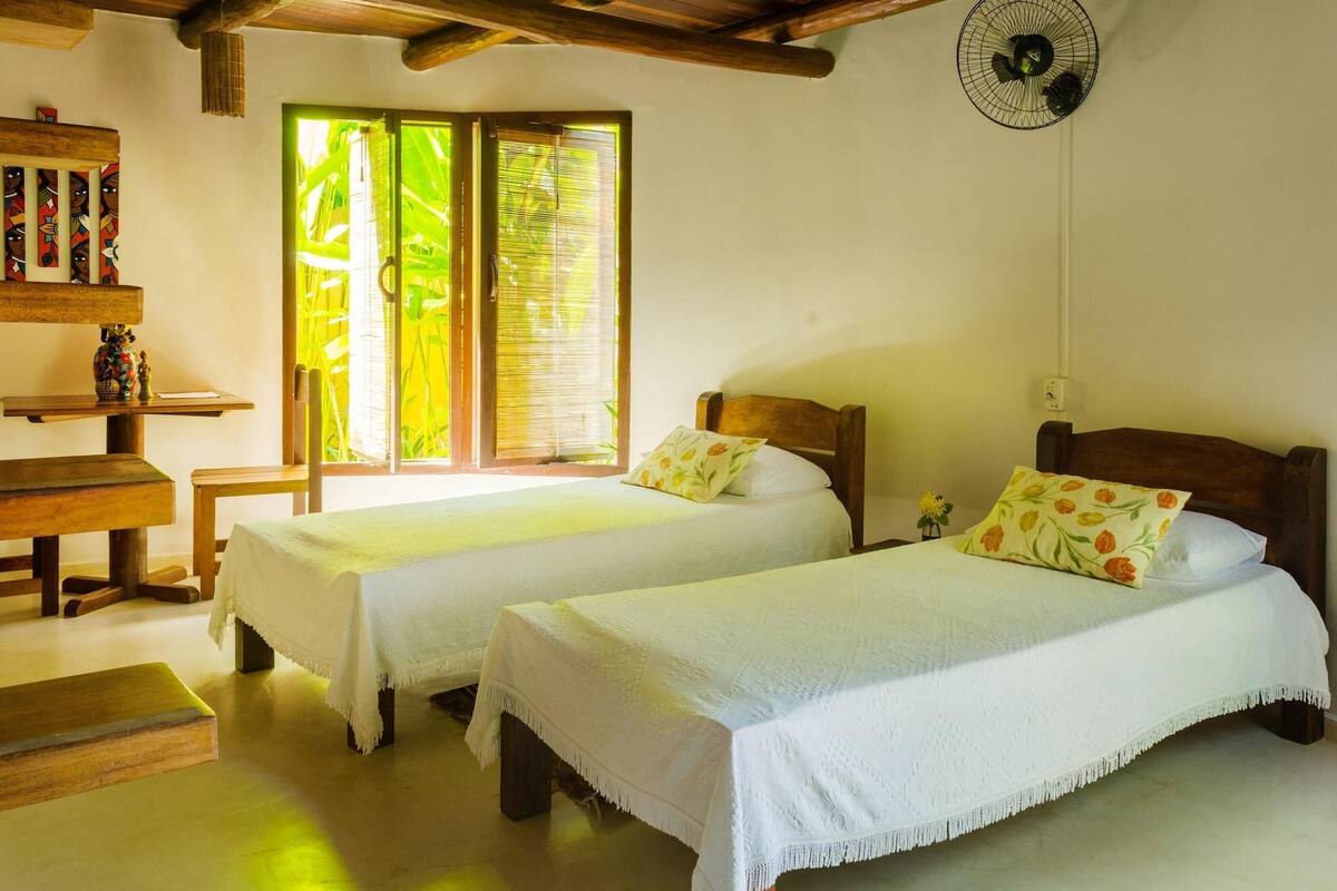 Ein Zimmer mit zwei Betten, einem Holztisch und einem Ventilator.