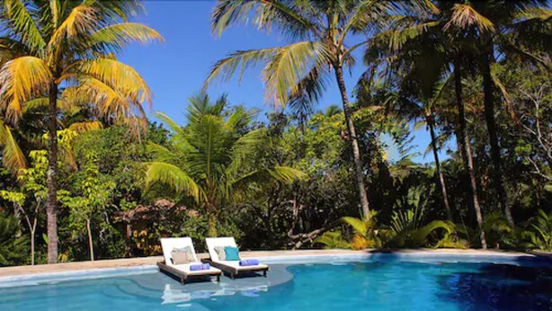 A pool with lounge chairs and palm trees. - Pousada Jacarandá (Porto Seguro)