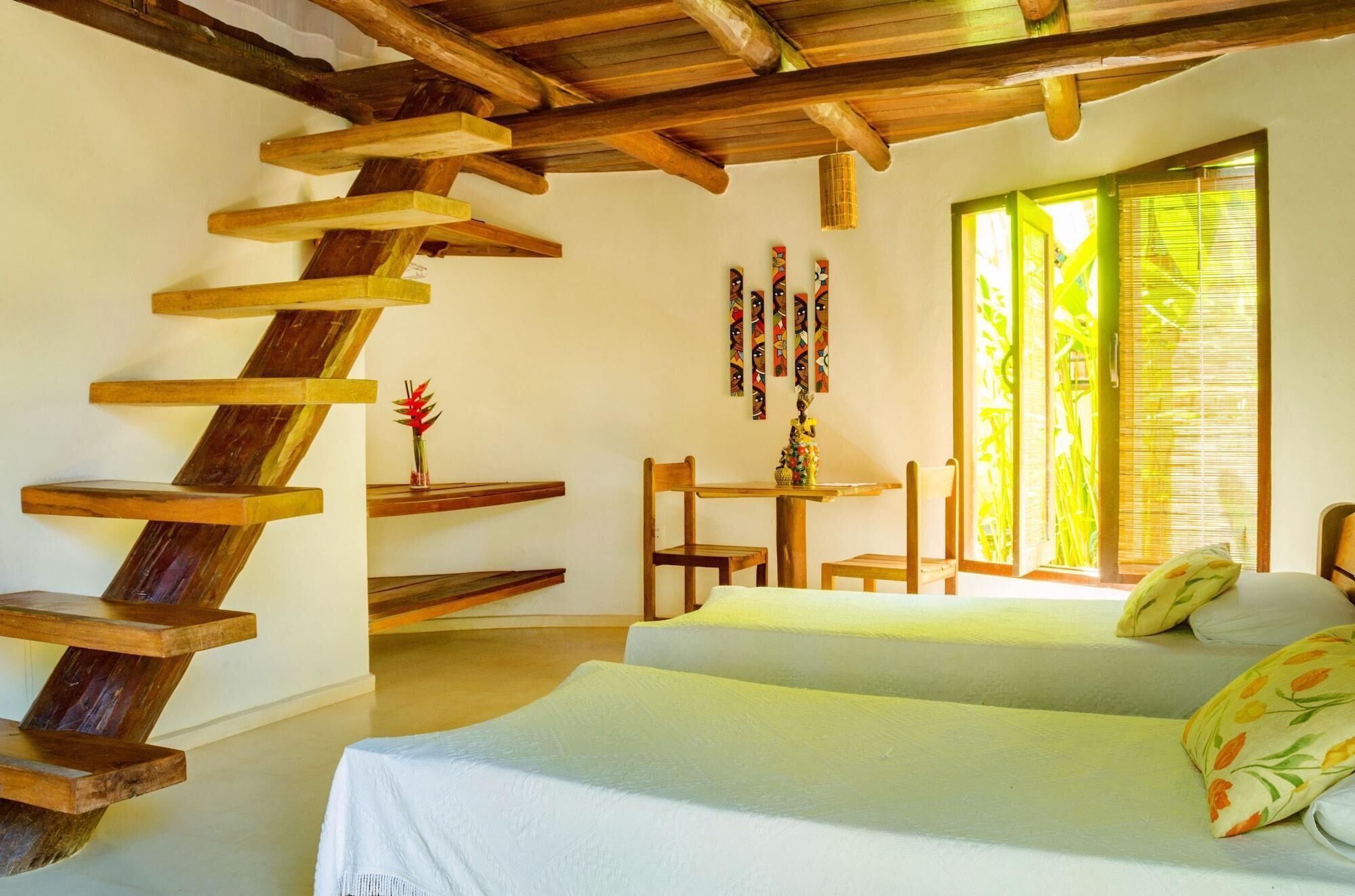 Ein Zimmer mit einer Wendeltreppe aus Holz, zwei Betten, einem kleinen Tisch mit Stühlen und einem Fenster mit Jalousien.