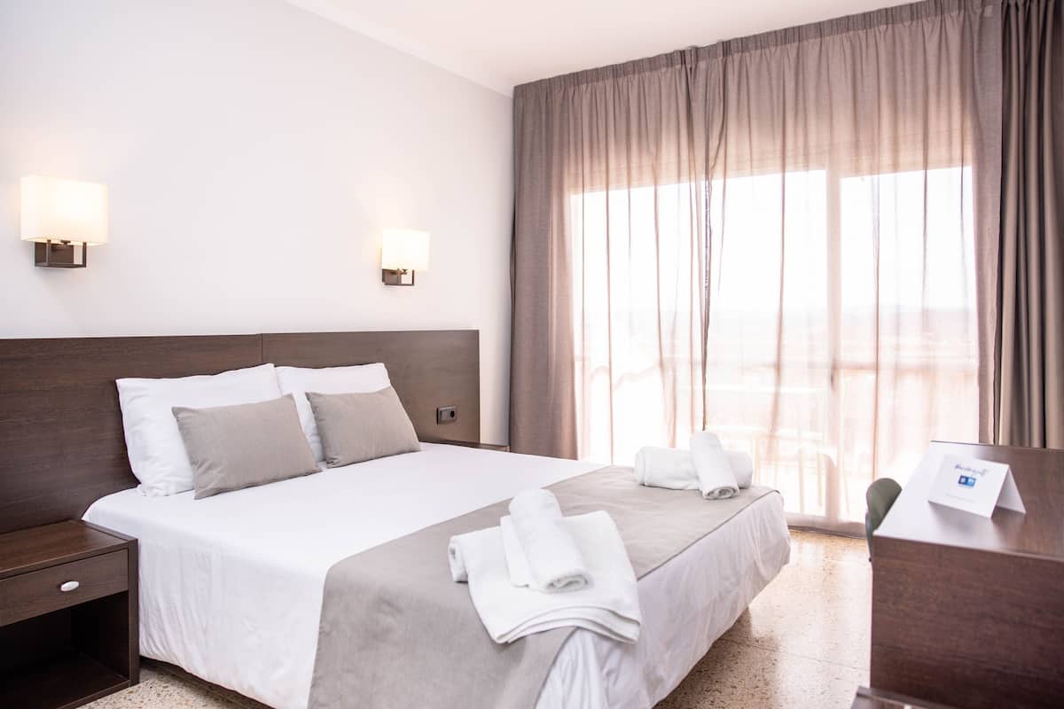 A hotel room with a large bed, two bedside tables, a desk, and a window with curtains.