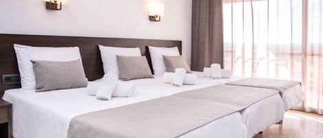 Habitación de hotel con una cama grande, dos lámparas de pared, vistas al exterior y una ventana con cortinas.