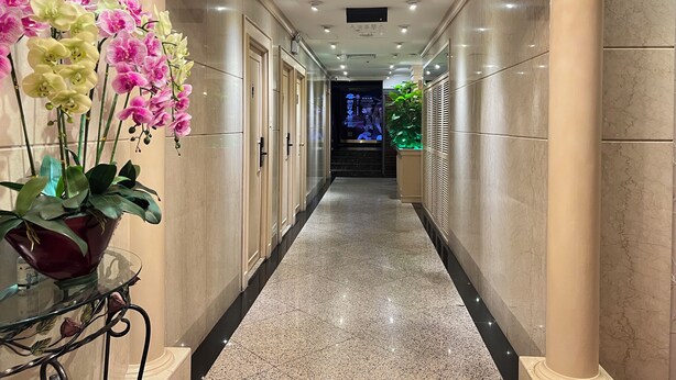 Un pasillo con suelo de mármol, columnas y una mesa de cristal con flores.