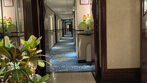 Pasillo de hotel con alfombra azul, plantas en macetas y una recepción con un número de teléfono.