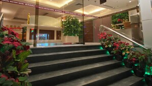 Entrada de un hotel con una escalera, puertas de cristal y plantas de interior.